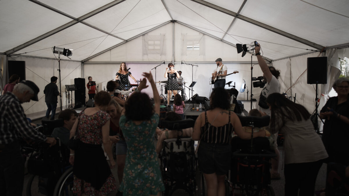 Un concert sous une tente. Dans le public, plusieurs personnes son en fauteuil roulant