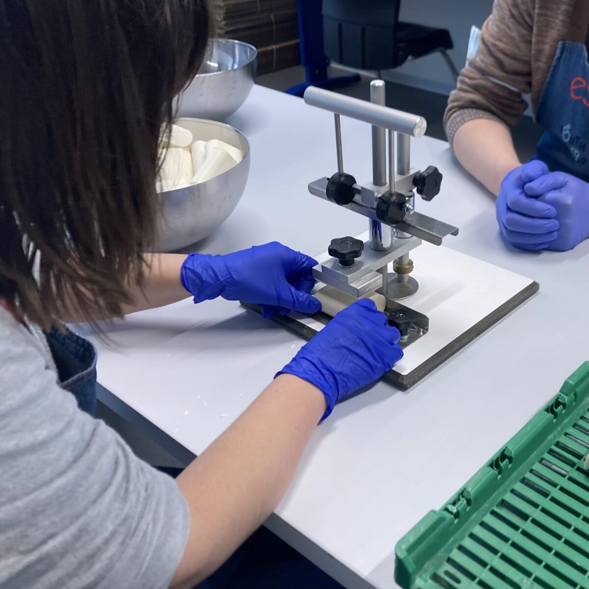 Deux personnes les mains gantées fabriquent du savon. On ne voit pas leurs visages