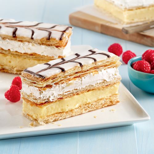 Une assiette blanche sur laquelle est posée un mille-feuille et des framboises fraîches.