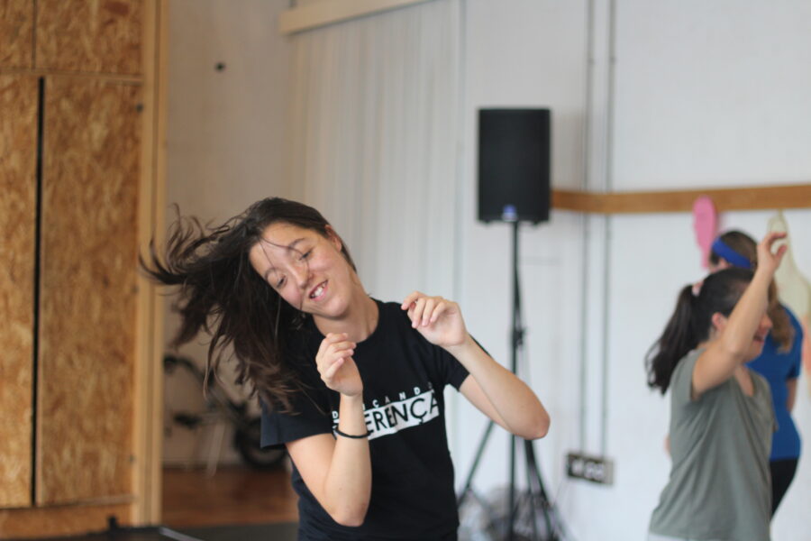 Une photo représentant quatre participantes et participants à l’atelier 1=1. Au premier plan, un participant dans un t-shirt de sport rose. Au second plan, trois autres participante et participants plus flou, qui semblent danser ou sautiller. On distingue un sourire sur le visage de l’un des participants.